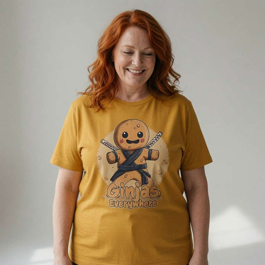 Red-haired woman smiling looking down in ochre Ginjas Everywhere t-shirt, funny ladies gingerbread graphic