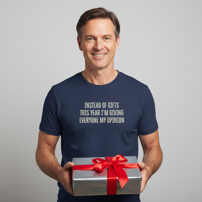 Man wearing a navy blue t-shirt with humorous text, holding a gift box with a red ribbon on a gray background.