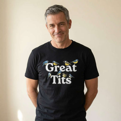 Grey-haired man with slight smile hands in pockets in black Great Tits tee, mens offensive rude bird pun