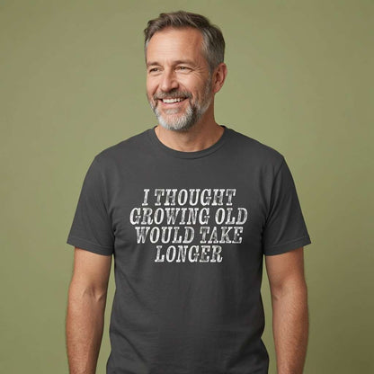 Grey-haired bearded man smiling in black I Thought Growing Old Would Take Longer tee, funny age related mens slogan