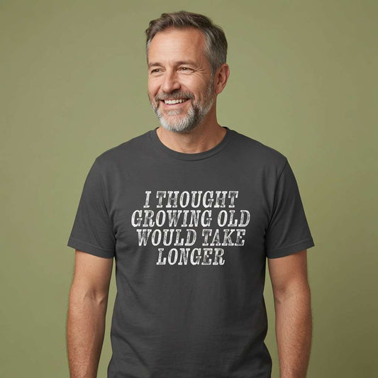 Grey-haired bearded man smiling in black I Thought Growing Old Would Take Longer tee, funny age related mens slogan