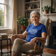 Woman sitting in a chair wearing a blue slogan t-shirt, in a cozy room with books and plants.