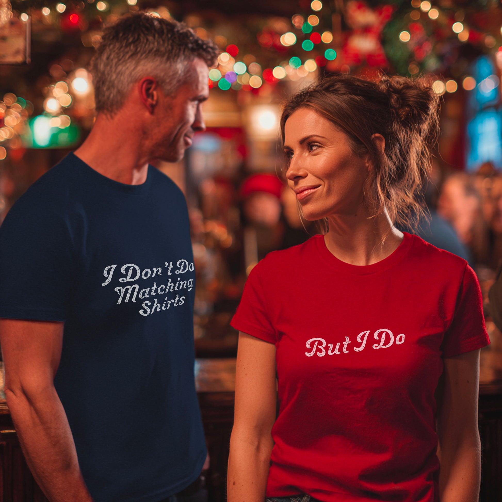Two people wearing matching shirts with humorous text in a festive setting.