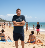Man standing on a beach wearing a t-shirt with the slogan 'yes i'm cold 24/7'