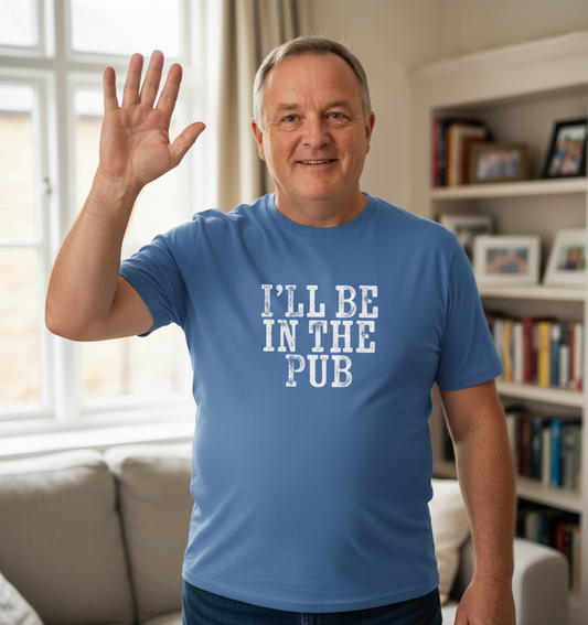 Man wearing a blue t-shirt with 'I'll Be in the Pub' text, waving in a living room.
