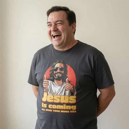 Man laughing in dark grey Jesus is Coming All Over Your Mum’s Tits tee with thumbs-up Jesus design, mens funny ultra offensive jesus graphic
