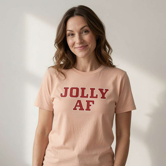 Woman with slight smile looking to the side in peach Jolly AF tee, witty ladies alternative christmas slogan