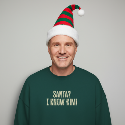 Man wearing a green sweater with 'Santa? I know him!' text and a festive hat on a gray background