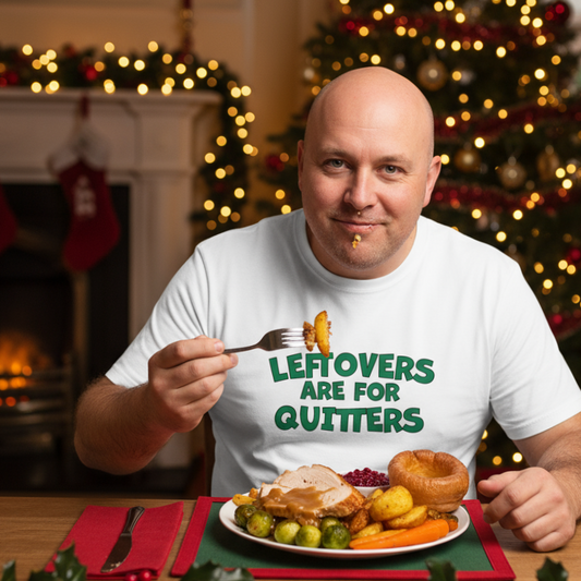 Man wearing a 'Leftovers are for Quitters' shirt in a festive setting with a Christmas tree and fireplace.
