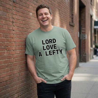 Man laughing leaning against brick wall in aloe Lord Love a Lefty tee, slogan