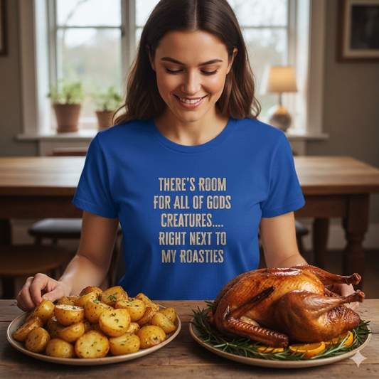 Woman in a blue t-shirt with a humorous text design, standing next to roasted potatoes and a turkey on a table.