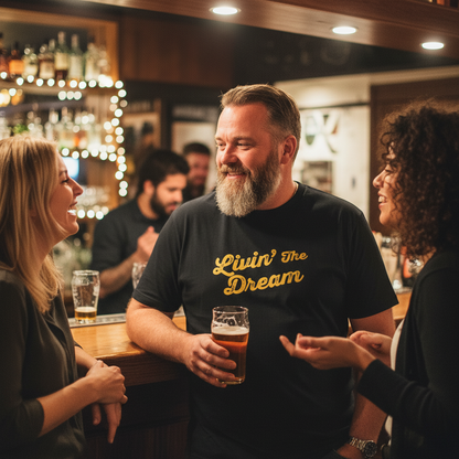 Man in a bar holding a beer, wearing a black t-shirt with 'Livin' The Dream' text.
