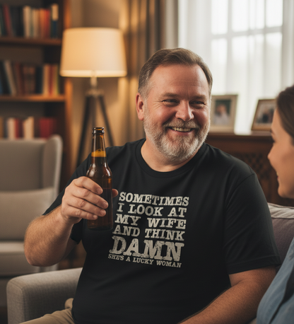 Man holding a beer bottle and wearing a humorous t-shirt in a cozy living room.