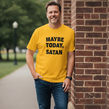 A man wearing a bright yellow t-shirt with the text 'MAYBE TODAY, SATAN' in black capital letters, standing outdoors next to a brick wall.