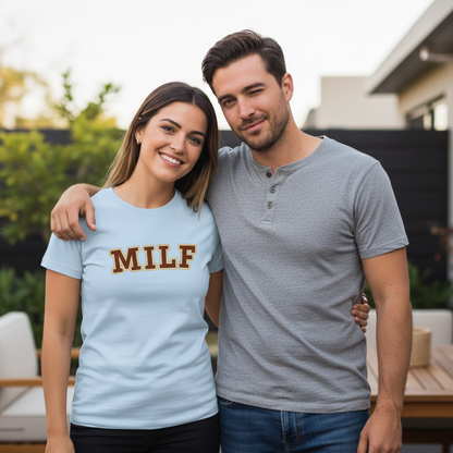 Man and woman standing together outdoors, woman wearing a light blue t-shirt with 'MILF' text.