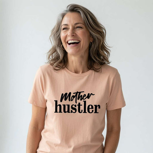 Woman laughing looking up in peach Mother Hustler t-shirt, ladies witty relatable busy mum slogan