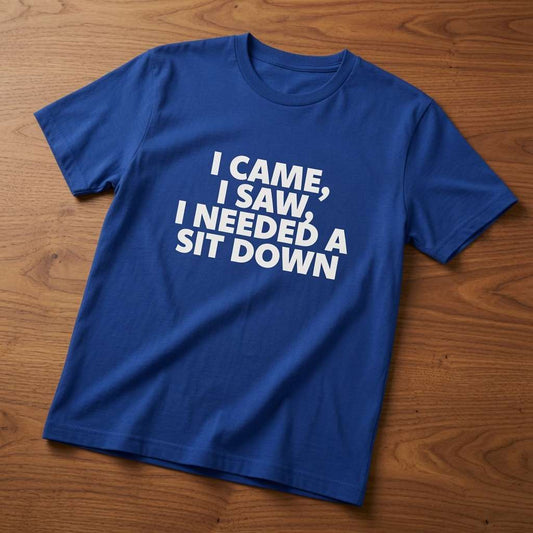 Royal blue I Came, I Saw, I Needed a Sit Down t-shirt laid flat on a wooden surface, simple white text that hits every bloke of a certain age right in the knees