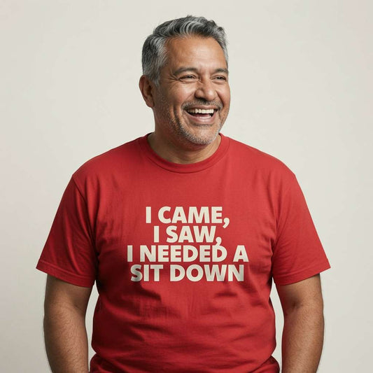 Older man with grey hair laughing heartily while wearing a bright red I Came, I Saw, I Needed a Sit Down t-shirt, classic witty banter about getting older