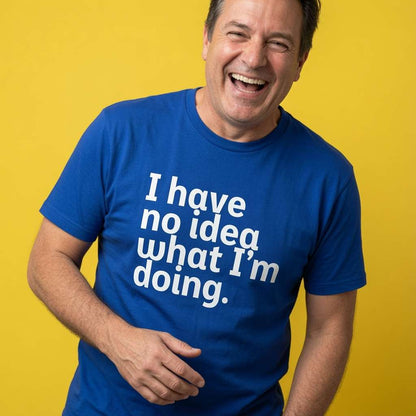Man laughing with one hand near his stomach while wearing a blue I Have No Idea What I’m Doing t-shirt, fun mens witty relatable statement design full of pure attitude