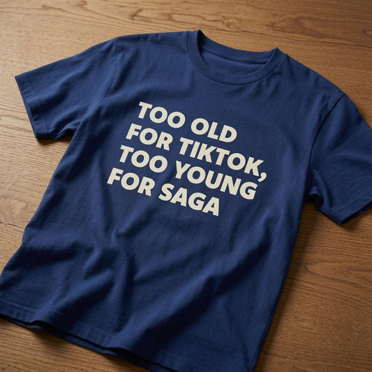 Navy blue Too Old For TikTok, Too Young For Saga t-shirt laid flat on a wooden surface, clean white text perfect for witty age-related gift