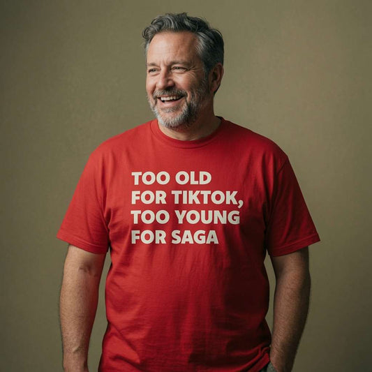 Bearded man smiling and looking slightly to the side while wearing a red Too Old For TikTok, Too Young For Saga t-shirt, humorous age-related slogan that hits the middle-aged sweet spot