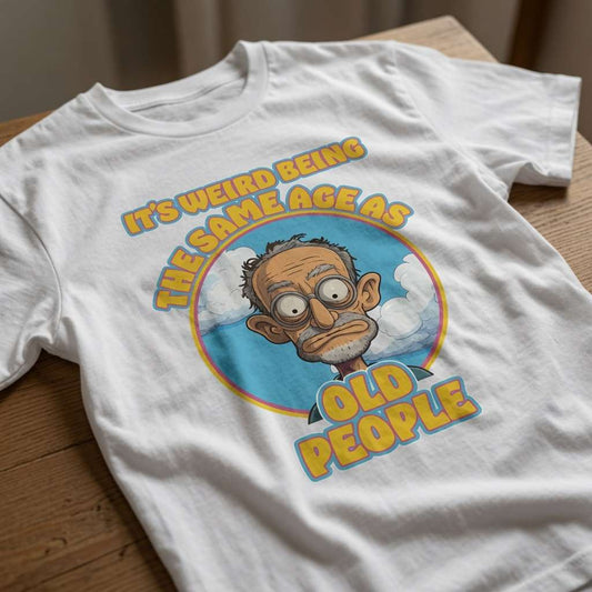 White It’s Weird Being The Same Age As Old People t-shirt laid flat on a wooden surface showing the full cartoon old man graphic, witty ladies old banter graphic design full of pure attitude