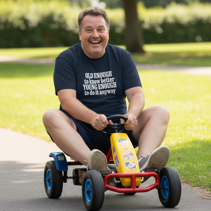 Man riding a small go-kart in a park wearing a t-shirt with a humorous quote.