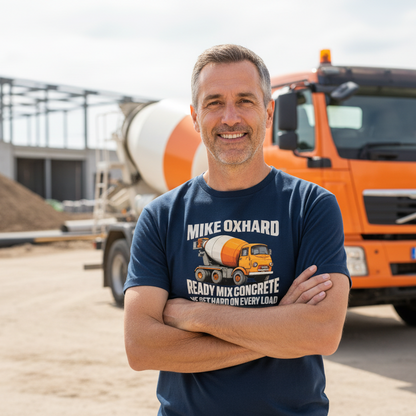 Man wearing a navy t-shirt with a cement mixer graphic and text, standing in front of an orange concrete truck on a construction site.