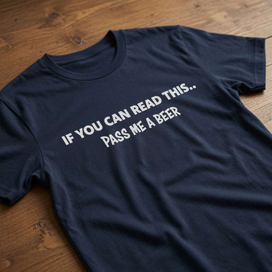 Navy blue t-shirt laid flat on a wooden surface with the white slogan “If You Can Read This... Pass Me A Beer”, classic mens dad quote pub banter design