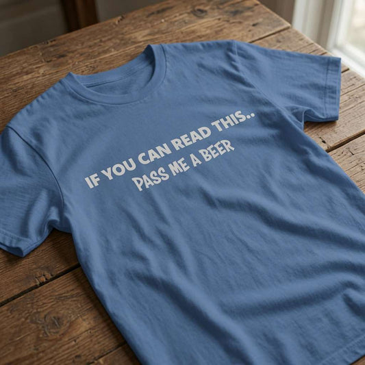 Blue t-shirt laid flat on a wooden table with the white slogan “If You Can Read This... Pass Me A Beer”, humorous ladies beer slogan perfect for pub banter