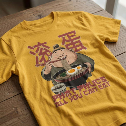 Yellow Phat Phucs t-shirt laid flat on a wooden table featuring a cartoon man slurping noodles with Chinese characters and the slogan “All You Can Eat”, funny Chinese writing graphic design