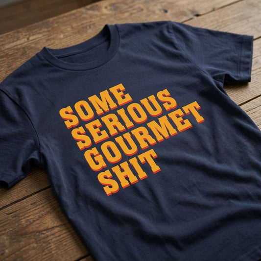 Navy blue Some Serious Gourmet Shit t-shirt laid flat on a wooden surface with bold orange and yellow text, fun mens movie-inspired quote design