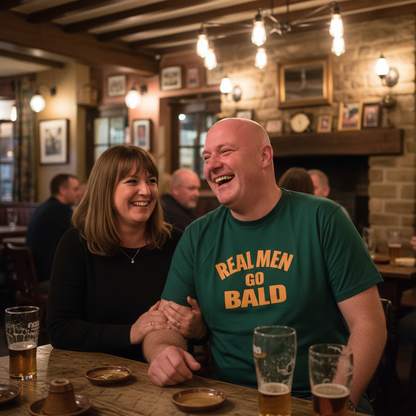 Two people sitting at a bar, one wearing a 'Real Men Go Bald' shirt, with drinks on the table.