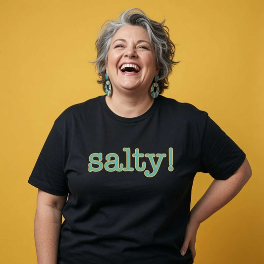 Woman with grey hair laughing in a black Salty! t-shirt, funny ladies witty bitchy text that every confident woman will claim
