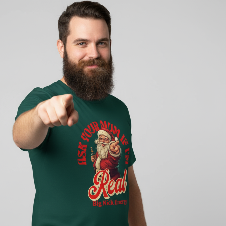Man wearing a green funny santa t-shirt with a graphic design and the slogan "Ask your mum if i'm real, Big nick energy" pointing forward on a gray background