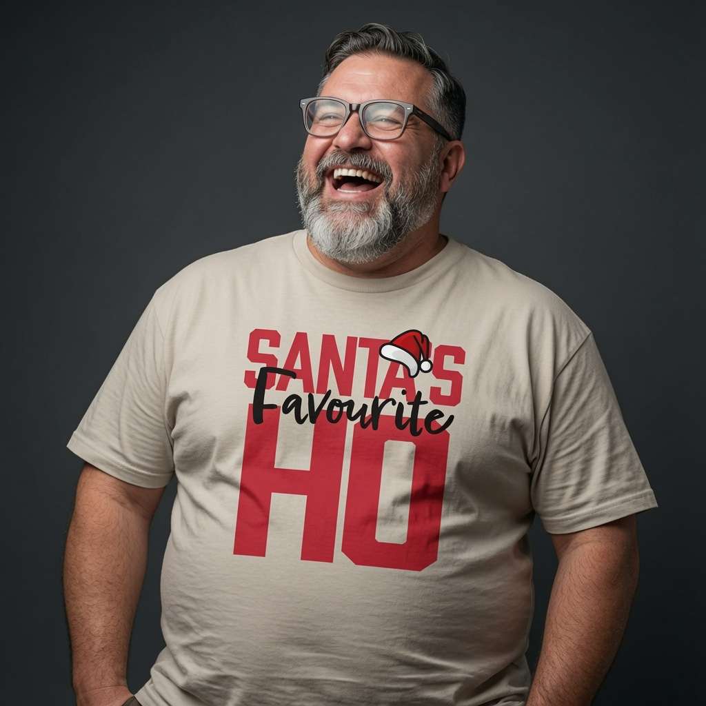 Bearded man with glasses laughing while wearing a beige Santa’s Favourite HO t-shirt with a little Santa hat on the text, funny mens witty xmas banter slogan