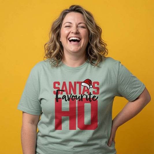 Woman laughing with hands on her hips while wearing a light green Santa’s Favourite HO t-shirt, fun ladies xmas slogan design that every no-nonsense lady will claim