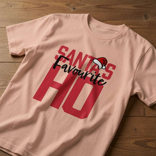 Peach Santa’s Favourite HO t-shirt laid flat on a wooden surface showing the full slogan with Santa hat, funny ladies xmas banter slogan design full of pure attitude