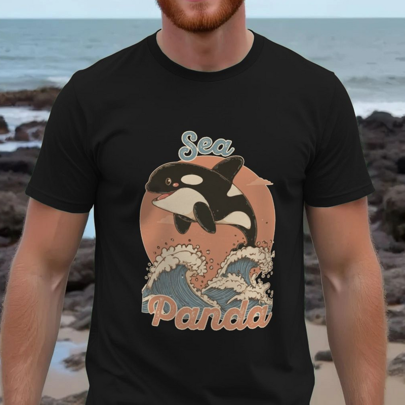 Person wearing a black t-shirt with a 'Sea Panda' design featuring an orca and waves, standing on a rocky beach.