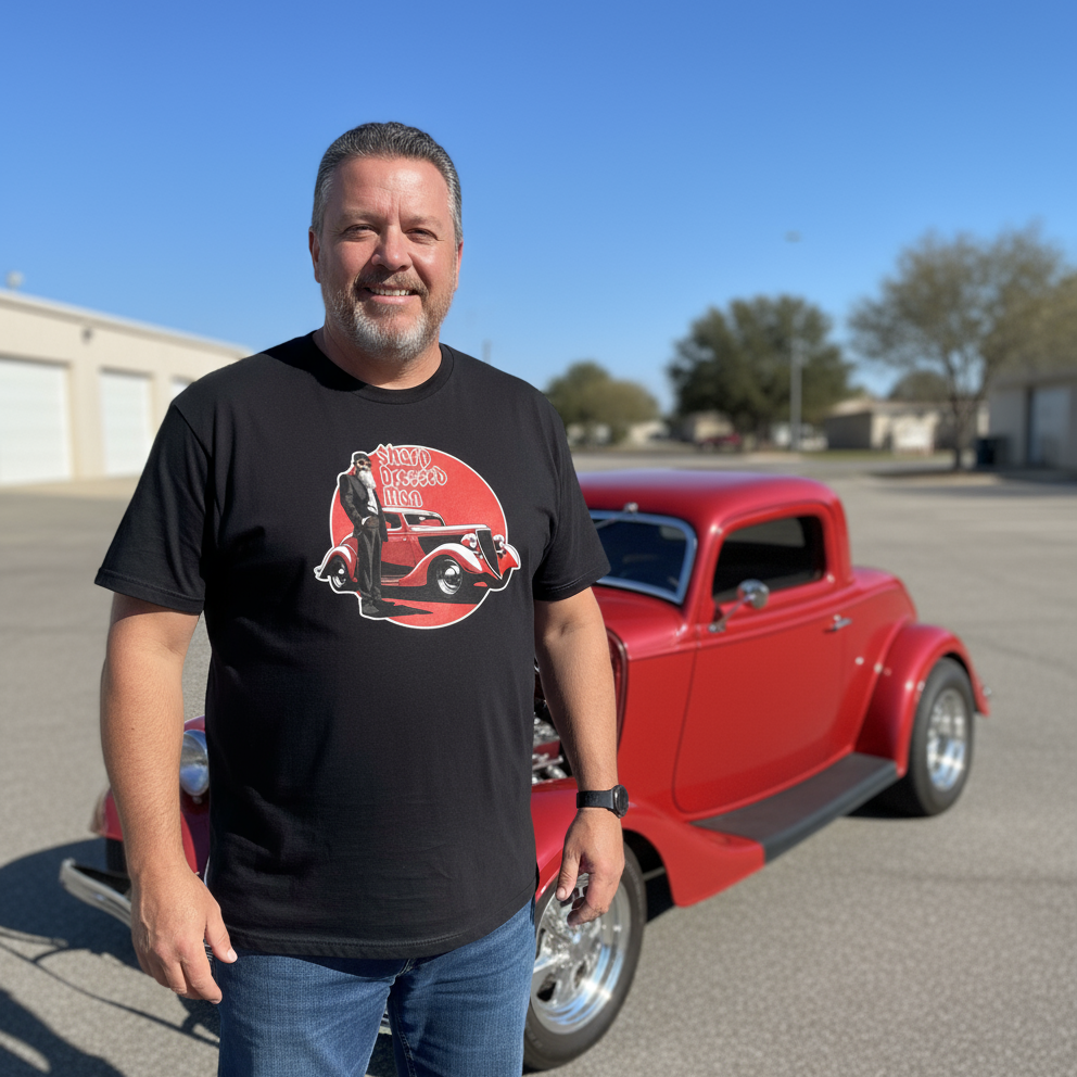 Man wearing a black t-shirt with a graphic design standing next to a red classic car.