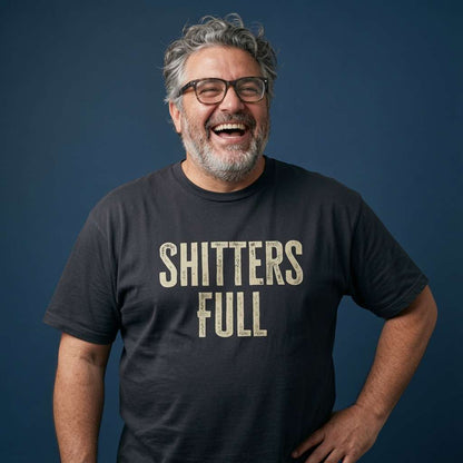 Bearded man with glasses laughing while wearing a black Shitters Full t-shirt, funny mens xmas film slogan full of pure festive attitude
