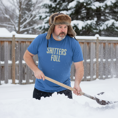 Man shoveling snow wearing a blue t-shirt with text and a fur hat in a snowy backyard.