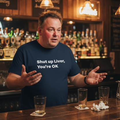 Man in a bar wearing a shirt with a humorous message, surrounded by drinks and bar decor.
