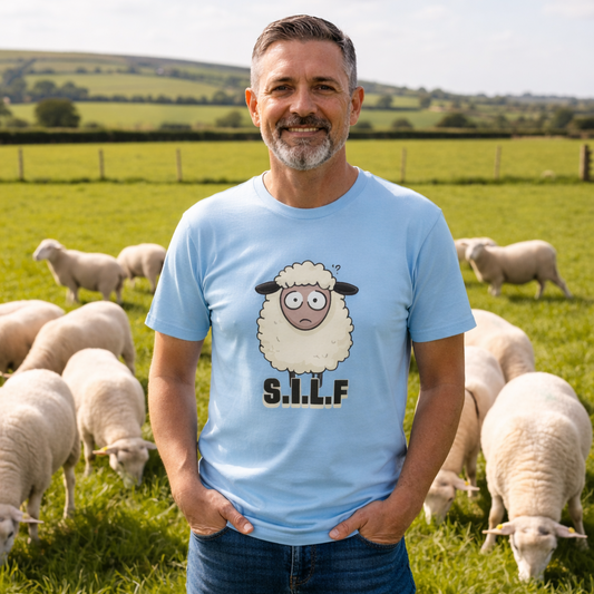 Man wearing a light blue t-shirt with a sheep graphic and 'S.I.L.F.' text, standing in a field with sheep.