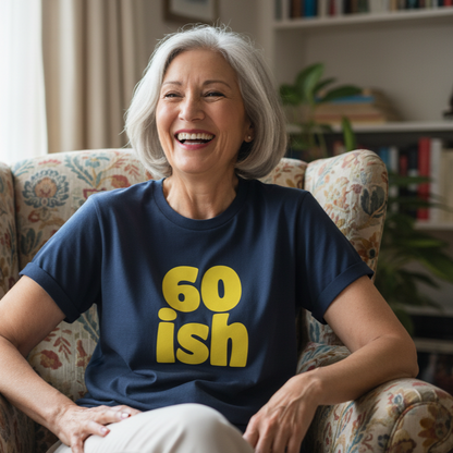 woman sat in a comfy chair wearing a navy t-shirt with the words '60 ish' in yellow writing