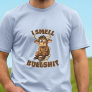 Light blue fun t-shirt with a cartoon bull on a toilet and text 'I Smell Bullshit' against a blue and green background.