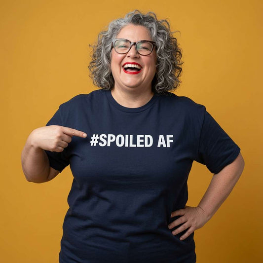 Grey-haired woman with glasses laughing and pointing at the text while wearing a navy #Spoiled AF t-shirt, funny ladies matching slogan