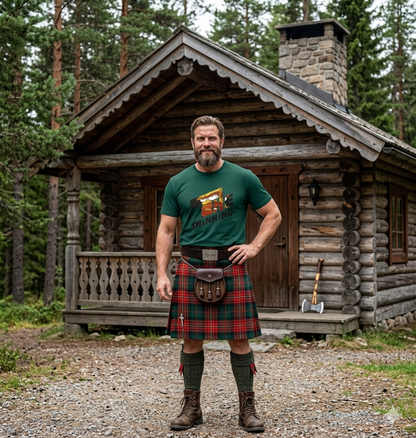 Man wearing a green t-shirt and red tartan kilt standing in front of a wooden cabin in a forest.