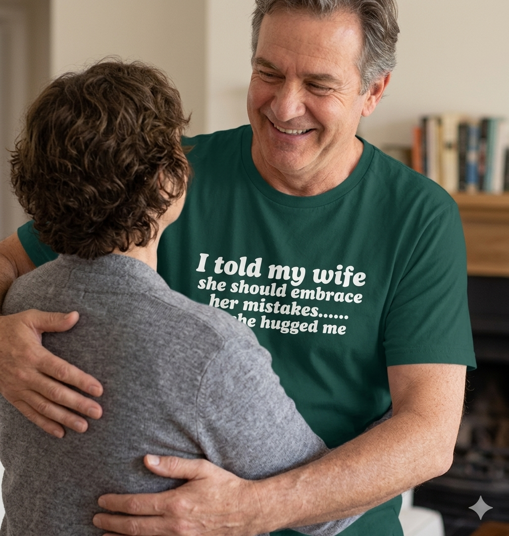 Man wearing a green t-shirt with humorous text hugging another person indoors.