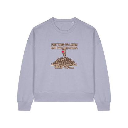 lavender christmas sweater with the graphic of rudoph stood ontop of a pile of reindeer and the slogan 'they used to laugh and call him names used to ..'